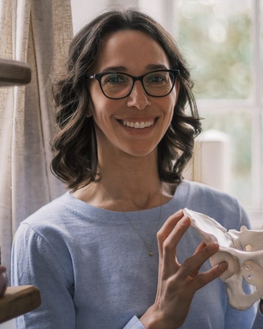 Shannon smiling, holding the model pelvis she uses in classes